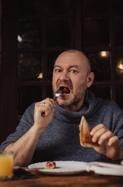 The man is having breakfast An ordinary middleaged man in a sweater is preparing to eat a sandwich in a dark room