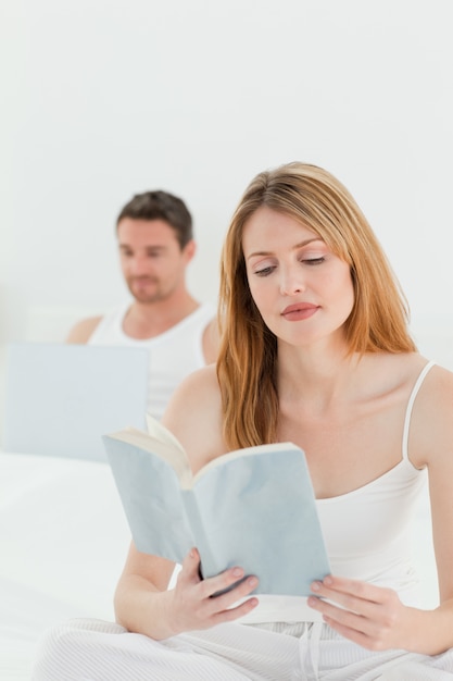 Man is on his laptop while his wife is reading a book