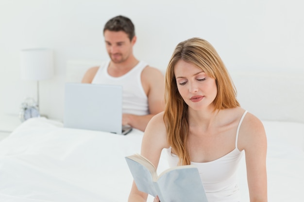 Man is on his laptop while his wife is reading a book