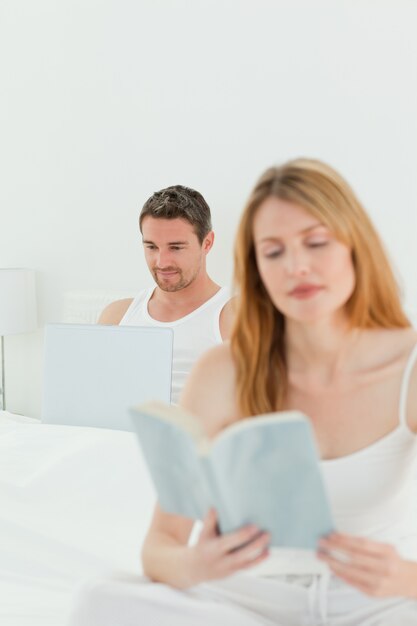 Man is on his laptop while his wife is reading a book