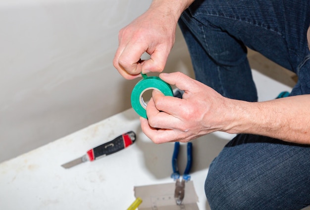 L'uomo tiene in mano del nastro adesivo isolante elettrico per lampadina lavori di riparazione di manutenzione nell'appartamento restauro al chiuso