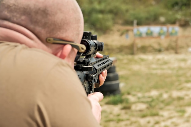 A man is holding an automatic weapon a man looks into the sight\
of a military weapon