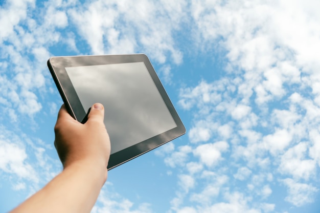 A man is holding a black tablet, against the background of the sky.