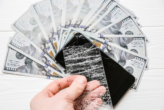 Man is holding broken screen protector tempered glass Money lying near the phone Dollar notes