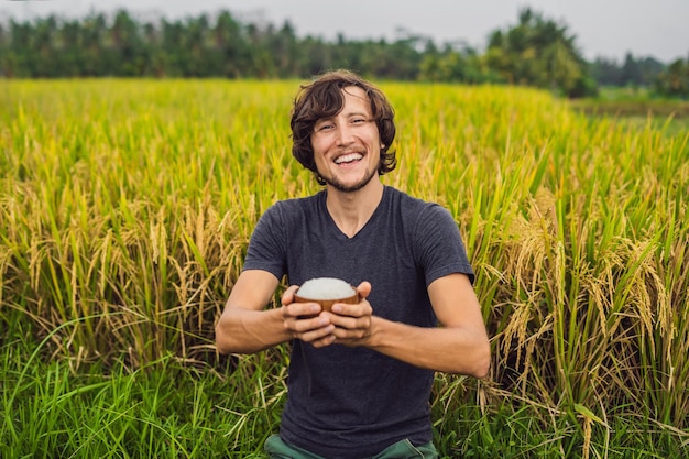 Man is holding a cup of boiled rice in a wooden cup on the background of a ripe rice field.
