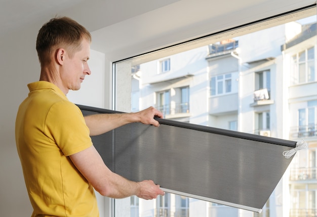 Man is holding fabric window blind gray.