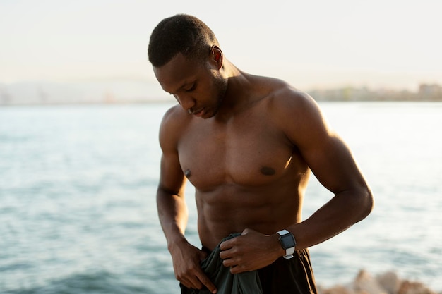 Photo man is holding his t shirt while standing at the beach with beautiful ocean at the background