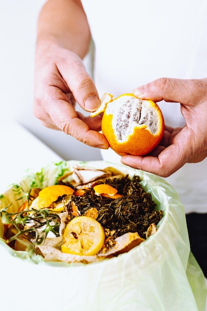 A man is holding an orange in a trash bag with a green bag full of food.