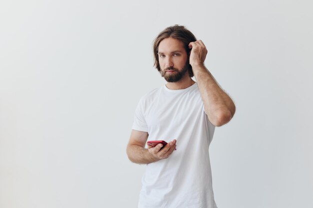 A man is holding a phone with wireless headphones in his ears and reading a social media message online freelancer job correspondence on a white background High quality photo