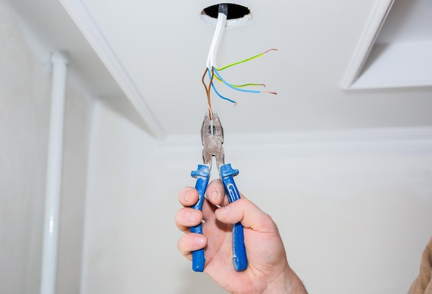 Photo man is holding pliers in his hands electrical insulator for light bulb adhesive tape for maintenance repair works in the flat restoration indoors