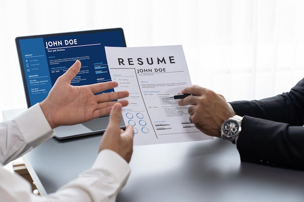 A man is holding a resume in front of a computer screen.