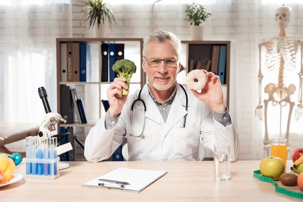 Man is Holding and Showing Broccoli and Donut.