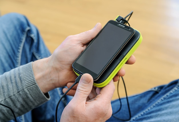 A man is holding a smartphone and a power bank.