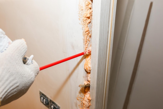 Man is installing the door with a spray foam repair works\
maintenance in the apartment