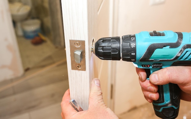 Man is installing the doors handle with a drill. Repair works. Maintenance in the apartment.