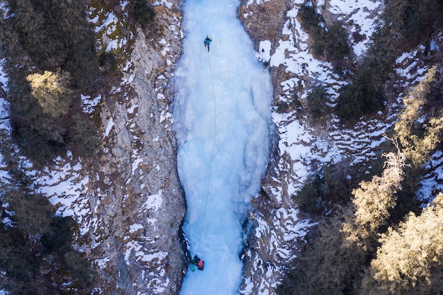 Foto l'uomo sta conducendo sul ghiaccio arrampicata su ghiaccio sulla cascata congelata vista aerea dall'alto barskoon valley kirghizistan