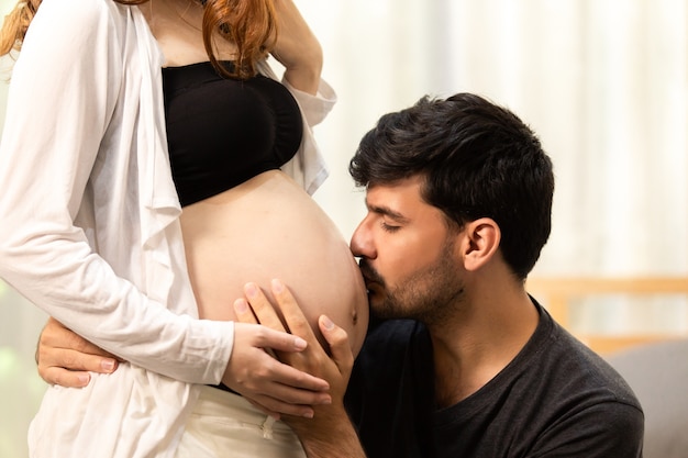 A man is listening to his beautiful pregnant wife's tummy and smiling