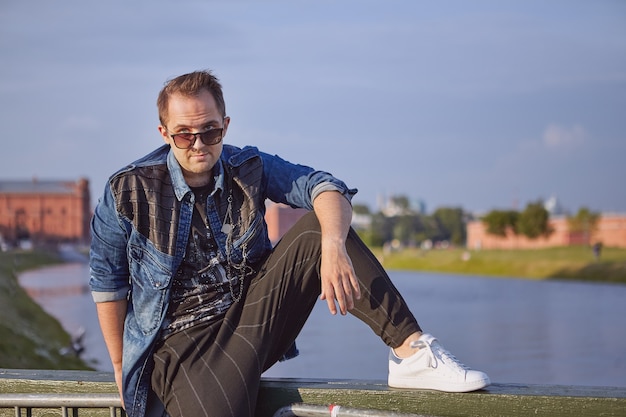 Man is looking out through sunglasses while sitting on the railing of bridge.