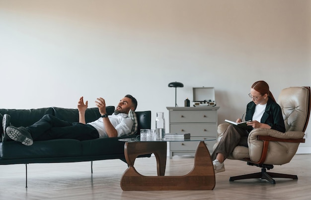 Photo man is lying down on the sofa session with woman psychologist