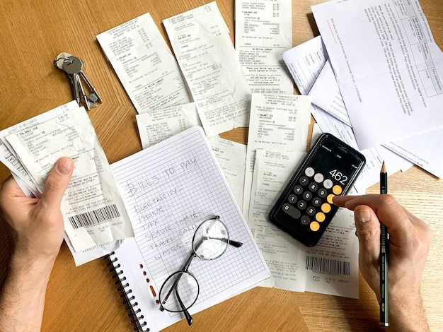 Man is making audit of household expenses using calculator and notebook lots of receipts and bills