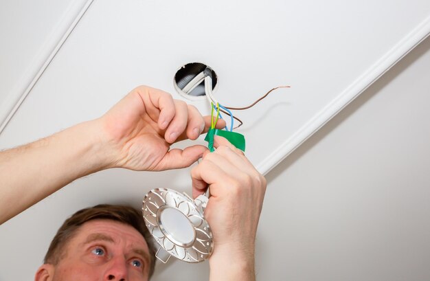 Man is making electrical insulator light bulb wires with\
adhesive tape maintenance repair works in the flat restoration\
indoors