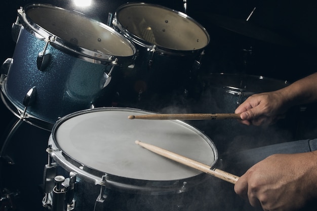 The man is playing drum set in low light background.