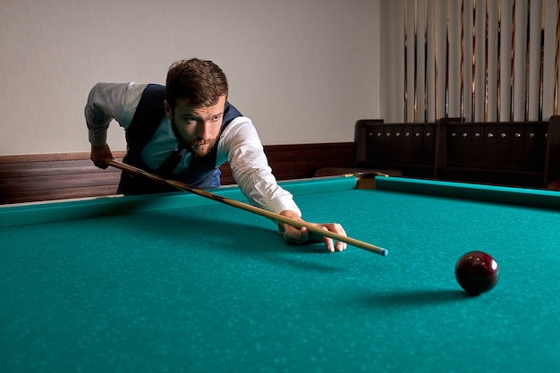 Man is playing snooker, he is aiming to shoot the snooker ball. handsome guy holds hands on snooker table. billiards