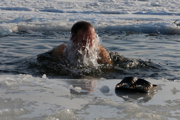 A man is plunged into an ice-hole.Bathing in ice water. The Baptism of Jesus. Religious holiday