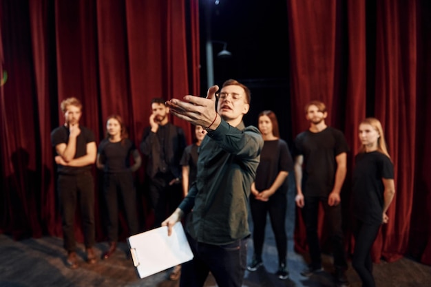 Man is practicing his role Group of actors in dark colored clothes on rehearsal in the theater