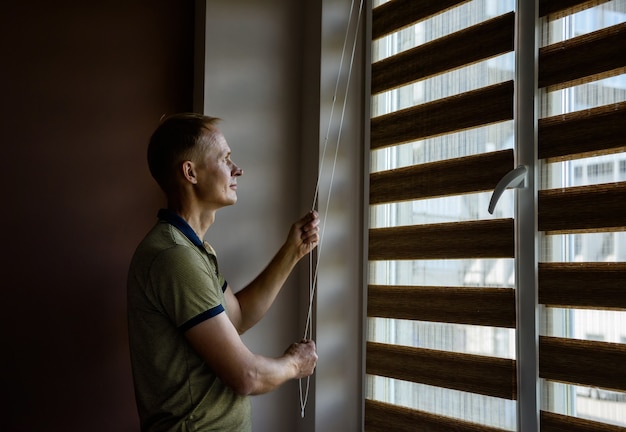 The man is pulling the chain to open the roller blinds.