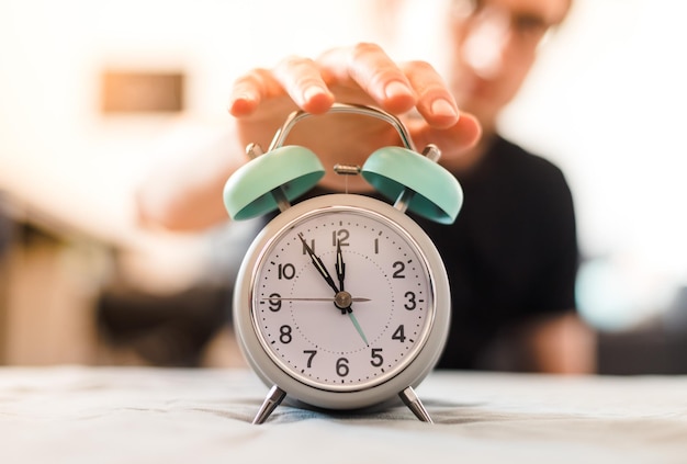 Man is pushing an alarm clock in the morning sunshine and blurry background