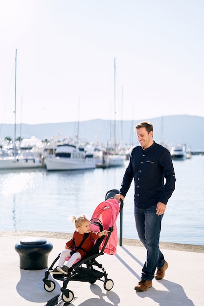 Man is pushing a pink stroller with his toddler sitting inside.  