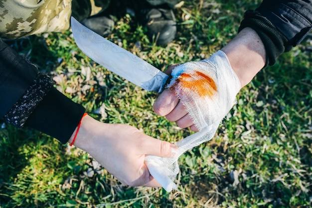 L'uomo sta mettendo un bendaggio sulla ferita sanguinante mano ferita tagliata con un coltello turista nella natura pericolo di infezione cure mediche