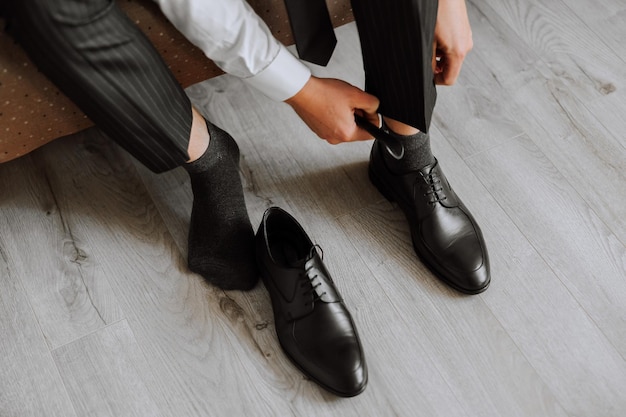 A man is putting on his shoes while sitting on a sofa in a hotel room A young entrepreneur is preparing to go on a business trip Businessman preparing for travel in home bedroom early in the morning