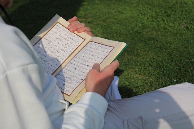 A man is reading a quran in a field