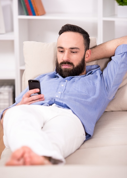 Man is relaxing on sofa and looking at cellphone