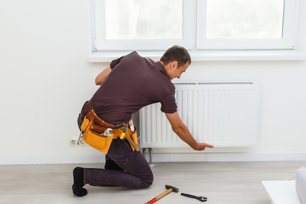 Man is repairing radiator battery in the room. Maintenance repair works renovation in the flat. Heating restoration. Wrench in hands.