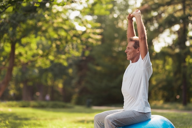 A man is sitting on the ball raising his hands up.