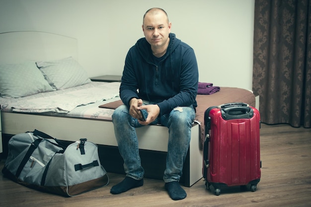 A man is sitting on a bed with a packed bag and a suitcase