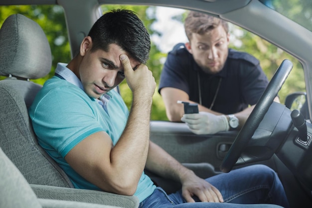 A man is sitting in a car and he is looking at his phone and he is wearing a blue shirt.