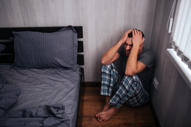 A man is sitting in a corner near the bed