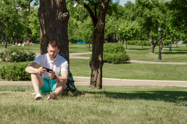 A man is sitting grass, workinga smartphone in a city parka green lawn outdoors in nature