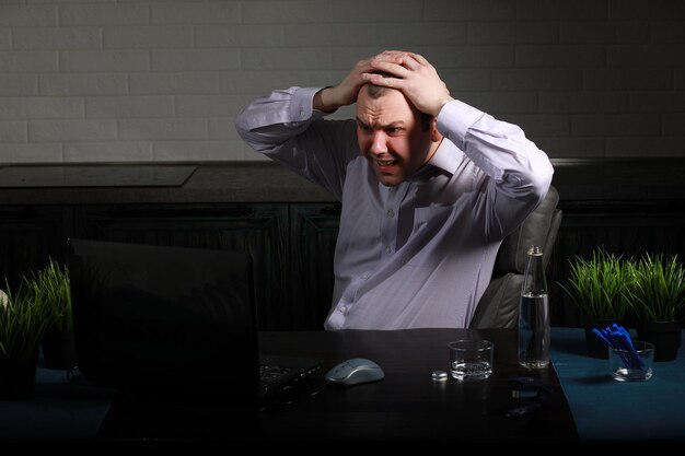 Man is sitting at his desk and working on a laptop