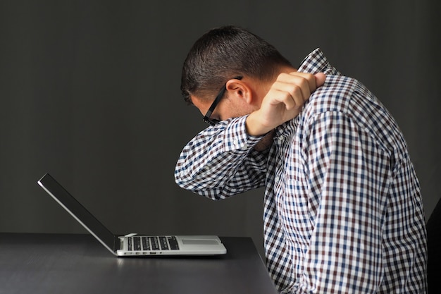 Man is sitting at his workplace with a laptop and sneezes into elbow. Concept stop spreading coronavirus.