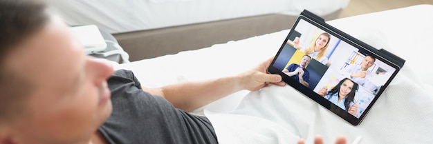 Un uomo è seduto in un letto d'albergo con un tablet che parla su una videoconferenza di primo piano con collegamento video