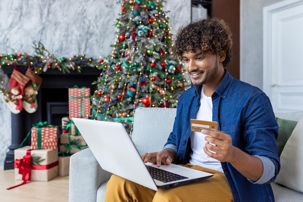 Man is sitting on a sofa in the living room of the house for christmas hispanic smiling satisfied