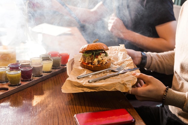 Un uomo è seduto a un tavolo con un gruppo di amici in possesso di una tavola di legno con un hamburger foto orizzontale