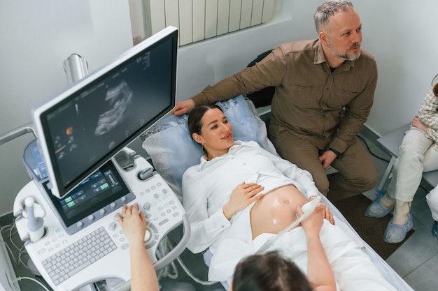 Foto un uomo è seduto con sua moglie una donna incinta è sdraiata in ospedale il dottore fa l'ecografia