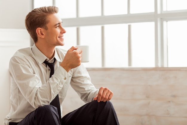 Man is smiling and holding a cup while sitting in room.