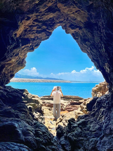 Foto un uomo è in piedi in una grotta e guarda l'oceano.